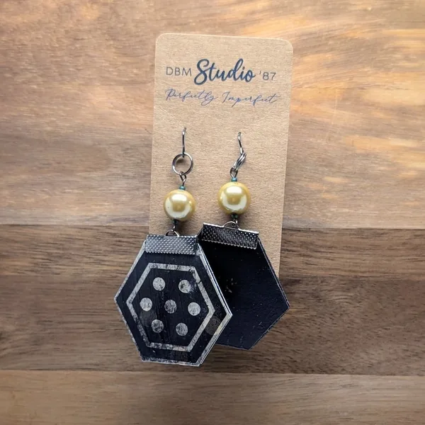 These medium octagon earrings feature a felt core, a durable Mod Podged finish, black polka‑dot and solid black designs, and are accented with black metal hardware and pearled beads for a lightweight, chic, and sophisticated accessory.